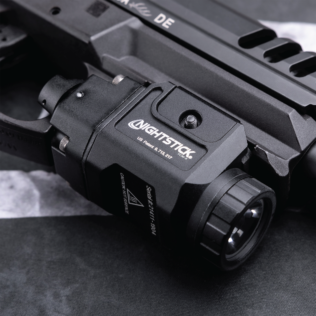 Close-up of a Nightstick flashlight attached to a firearm on a textured surface.