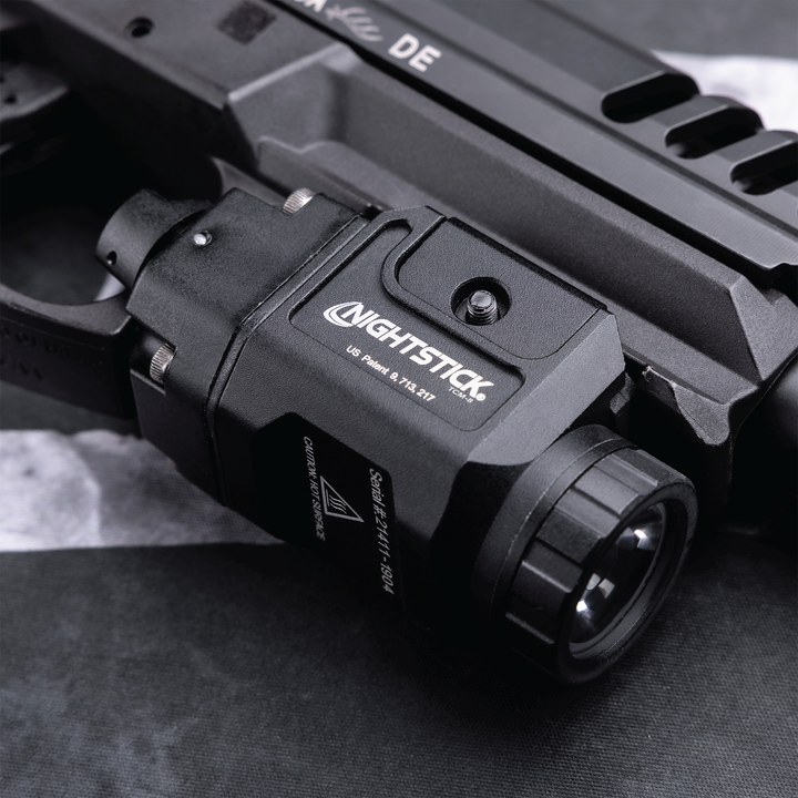 Close-up of a Nightstick flashlight attached to a firearm on a textured surface.